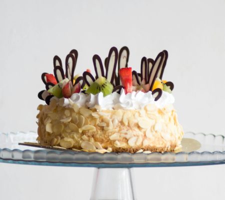 Delicious fruit-topped cake with almond slices and cream, perfect for celebrations.